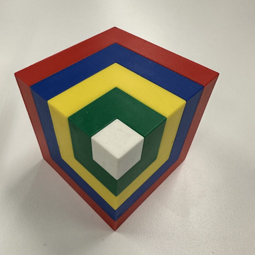 Layered cube shape made up of layers of five dfferent coloured cubes of increasing size, each larger cube surrounds the previous cube on the rear two sides and the bottom. The smallest cube is white. The next layer of the cube, surrounding the white cube, is green. The next layer of the cube is yellow. The fourth layer of the cube is blue. And the outermost layer of the cube is red.