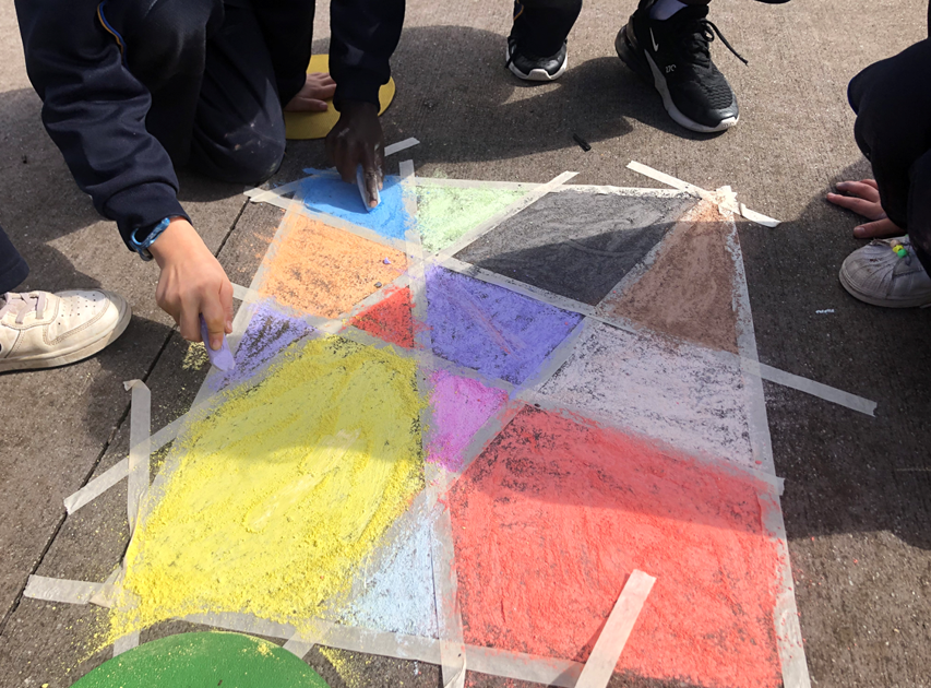 A group of people drawing on the ground to make angular coloured shapes like a stained glass window