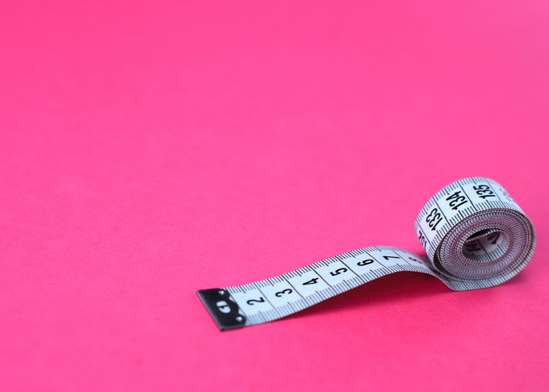 Image of a measuring tape on a pink background.