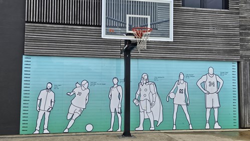 Outdoor basketball court in front of a mural with outlined figures